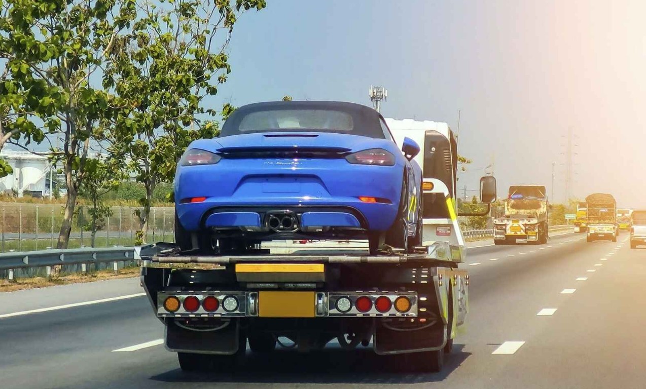 Flatbed tow truck transporting a blue sports car on the highway near West Islip, NY