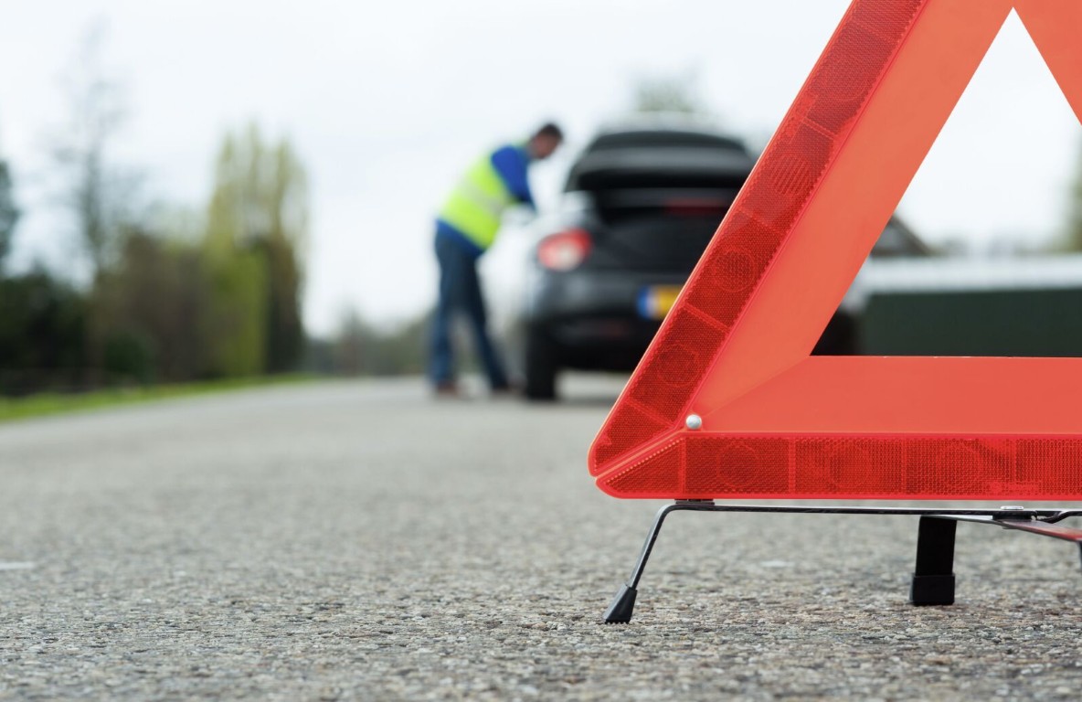 Roadside assistance technician setting up warning triangle near broken down car